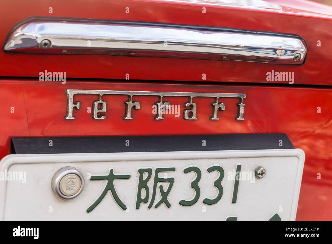 Detailansicht des Ferrari-Namensabzeichens und des Nummernschilds auf der Rückseite eines roten Sportwagens des Dino 246 GT aus den 1970er Jahren. Japanische Schrift liest Osaka. Stockfoto