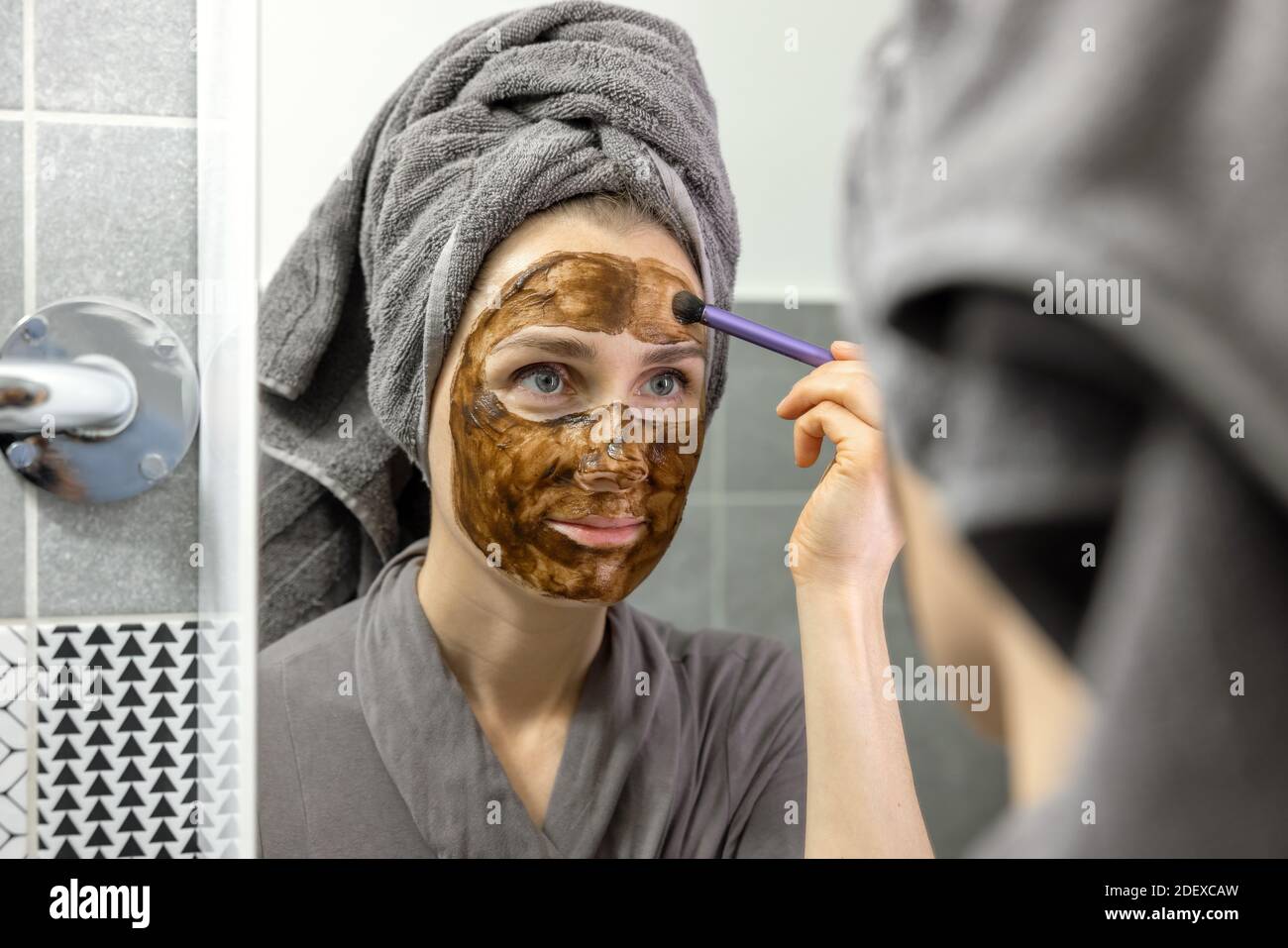 Frau Anwendung Schlamm Gesichtsmaske mit Pinsel vor dem Spiegel im Badezimmer zu Hause. Hautpflege Beauty-Behandlung Stockfoto