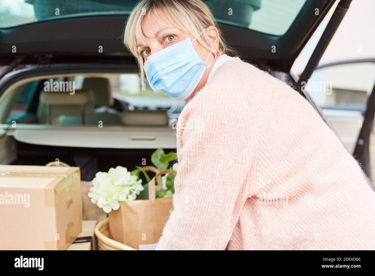 Frau mit Gesichtsmaske vor einem offenen Auto Trunk voller Pakete und Einkäufe Stockfoto