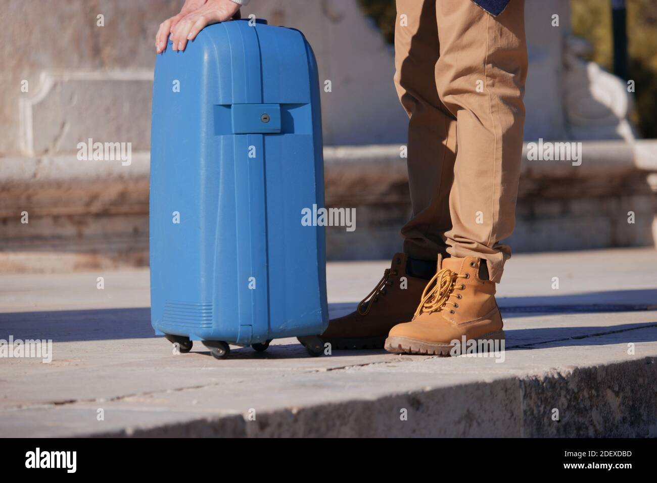 Nahaufnahme eines unerkennbaren jungen Mannes, der mit seinem Koffer in der Hand auf der Straße steht, müde nach einer langen Reise. Geschäftsreise 2021. Stockfoto