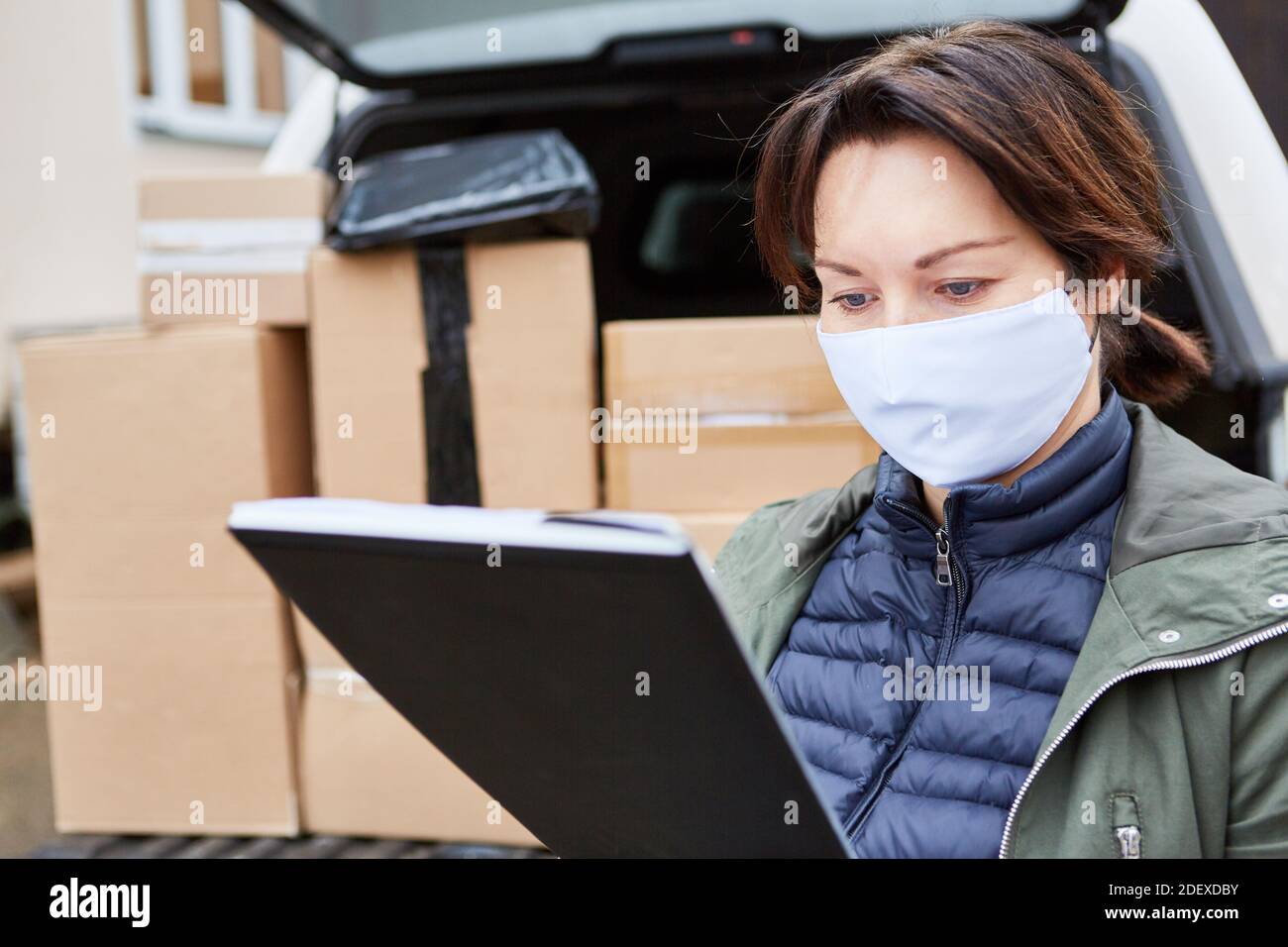 Lieferdienst Subunternehmer mit Gesichtsmaske prüft Lieferungen im Vorfeld Eines vollen Ladeplatzes Stockfoto