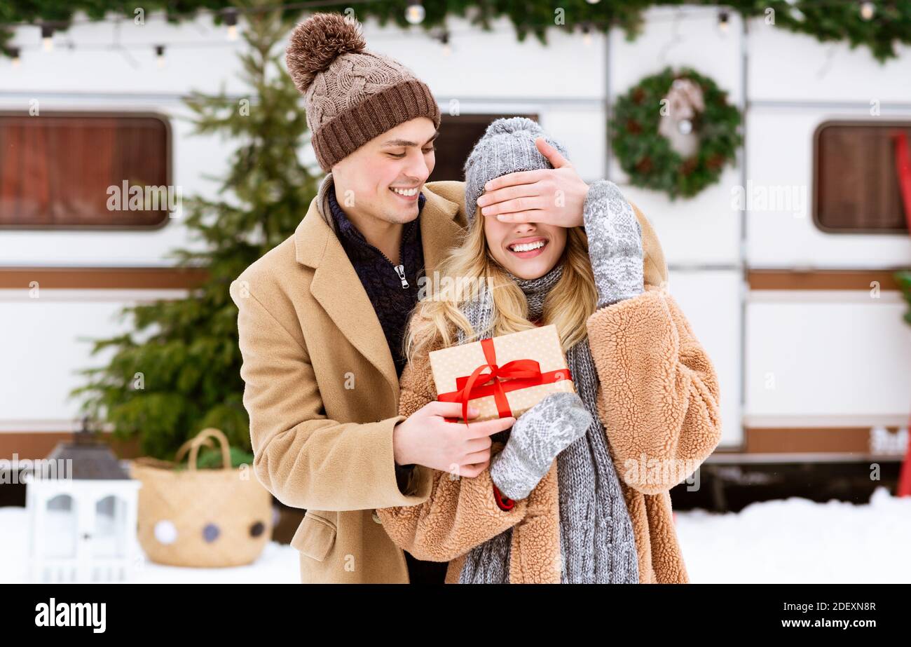 Weihnachtsüberraschung. Loving Young Guy Abdeckung Freundin Augen im Freien und geben Geschenk Stockfoto
