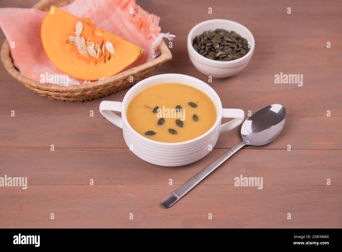 Weißer Teller mit Kürbispüree-Suppe, einem Stück Kürbis und Kürbiskernen auf Holzgrund. Stockfoto
