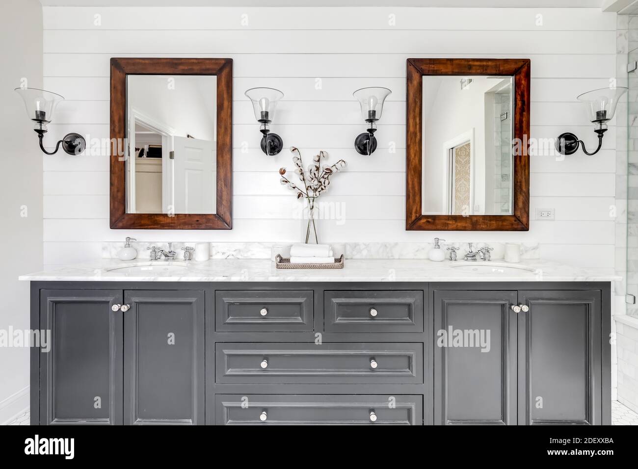 Ein luxuriös renoviertes Badezimmer mit einem grauen Kosmetikbereich, rustikalen Holzspiegeln sowie Chromhähnen und -Armaturen. Stockfoto