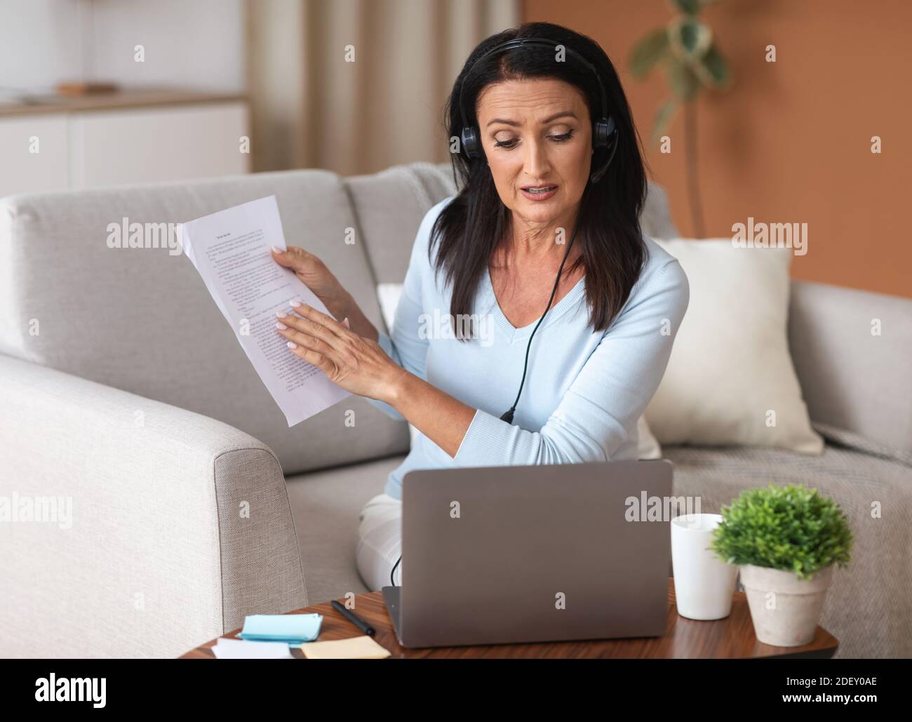 Frau im Headset sitzt am Schreibtisch, mit Videoclip auf Laptop Stockfoto