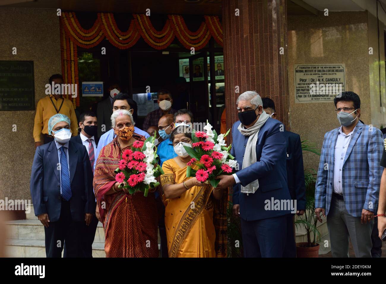 Eine Frau mit Gesichtsmast bietet dem Gouverneur Jagdeep Dhankar während der Einweihungszeremonie einen Blumenstrauß an.der Gouverneur von Westbengalen, Jagdeep Dhankar, eröffnet den Start des dritten Phase-Prozesses gegen Covaxine beim Indian Council of Medical Research (ICMR) in Kalkata. Stockfoto