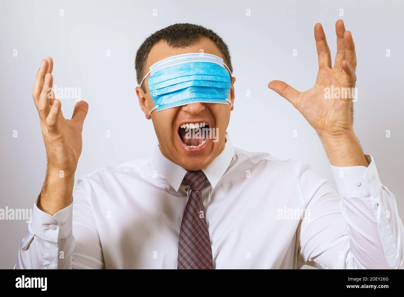 Ein Mann in einer Krawatte schreit mit einer medizinischen Maske auf die Augen. Konzept zum Thema Depression durch Coronavirus Stockfoto