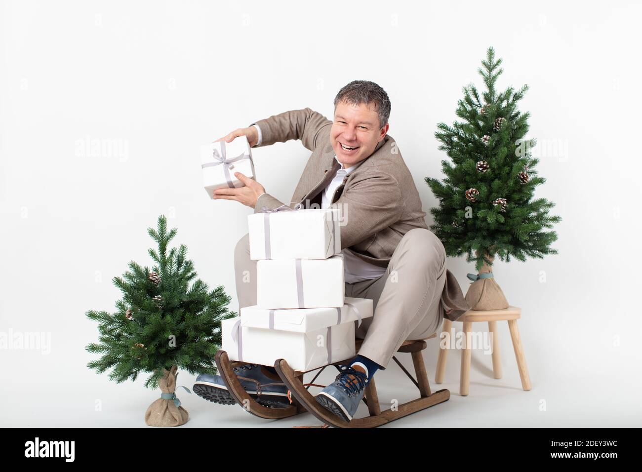 Weihnachten themed horizontal Business Porträt eines smart lässig gekleidet Männliche Führungskraft sitzt auf einem Schlitten jonglieren weiß verpackt Geschenk Boxen alle Set o Stockfoto