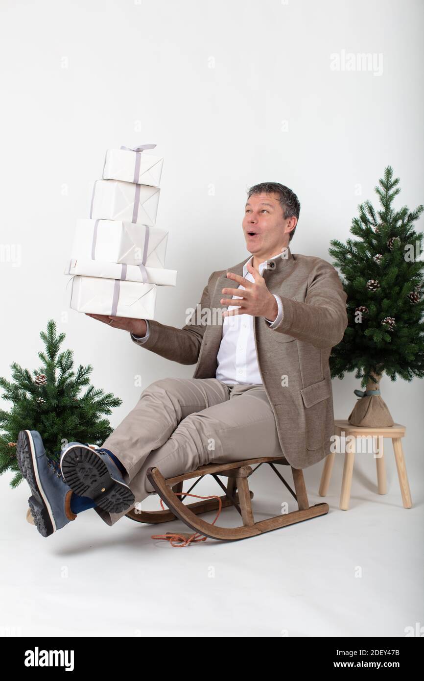Weihnachten themed horizontal Business Porträt eines smart lässig gekleidet Männliche Führungskraft sitzt auf einem Schlitten jonglieren weiß verpackt Geschenk Boxen alle Set o Stockfoto