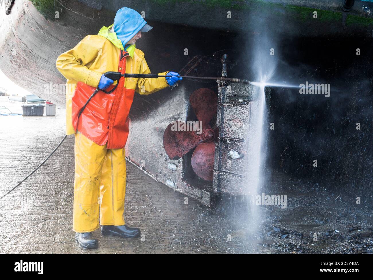 Kinsale, Cork, Irland. Dezember 2020. Fischer Michael McCarthy wäscht den Rumpf seines Fischerbootes 'Aurora Brealis', während er bei Ebbe an der Kaimauer in Kinsale, Co. Cork, Irland, gebunden ist. - Credit; David Creedon / Alamy Live News Stockfoto