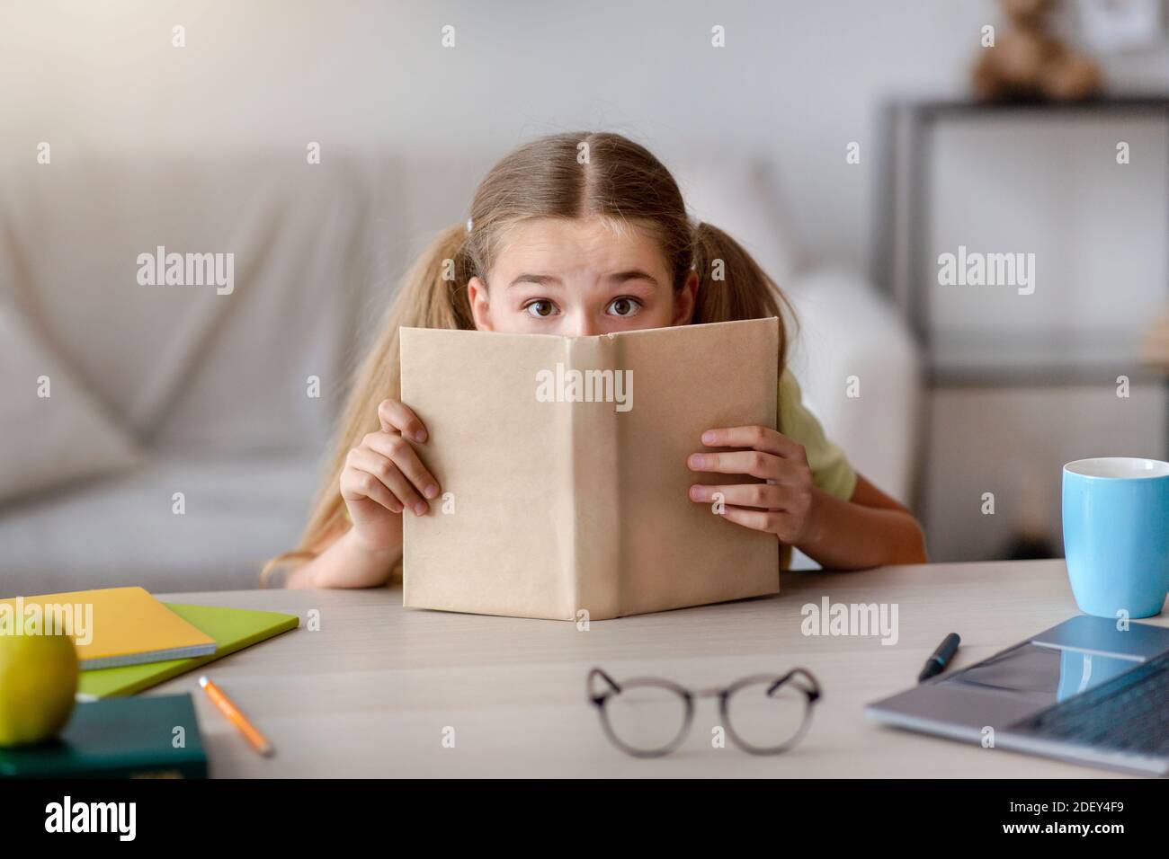 Verängstigte Mädchen mit weit offenen Augen versteckt hinter einem Buch Stockfoto