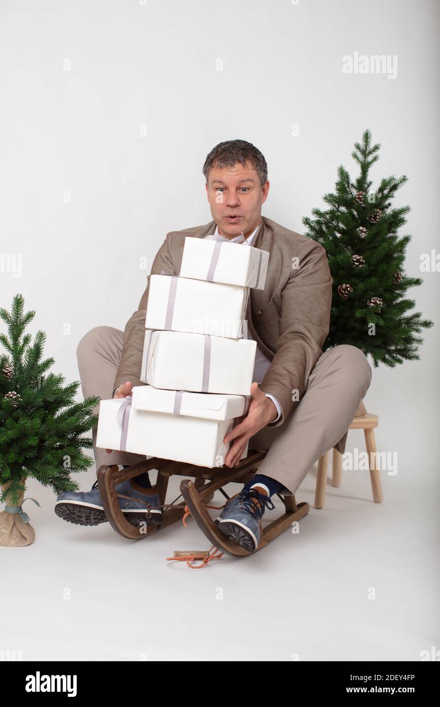 Weihnachten themed horizontal Business Porträt eines smart lässig gekleidet Männliche Führungskraft sitzt auf einem Schlitten jonglieren weiß verpackt Geschenk Boxen alle Set o Stockfoto