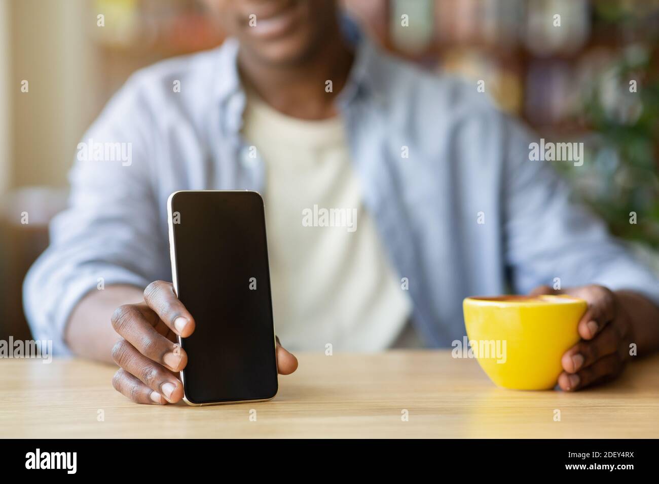 Beschnittene Ansicht der jungen schwarzen Kerl hält Smartphone mit leerem Bildschirm im Café, Mockup für mobile App-Design Stockfoto