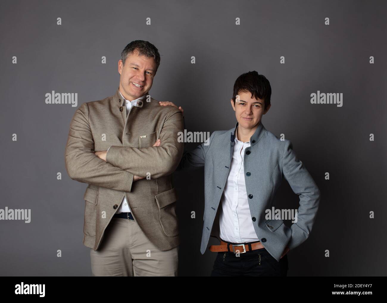 Horizontale Business-Paar Porträt gekleidet smart casual in blau, weiß, beige Hosen und Blazer auf grauem Hintergrund. Stockfoto