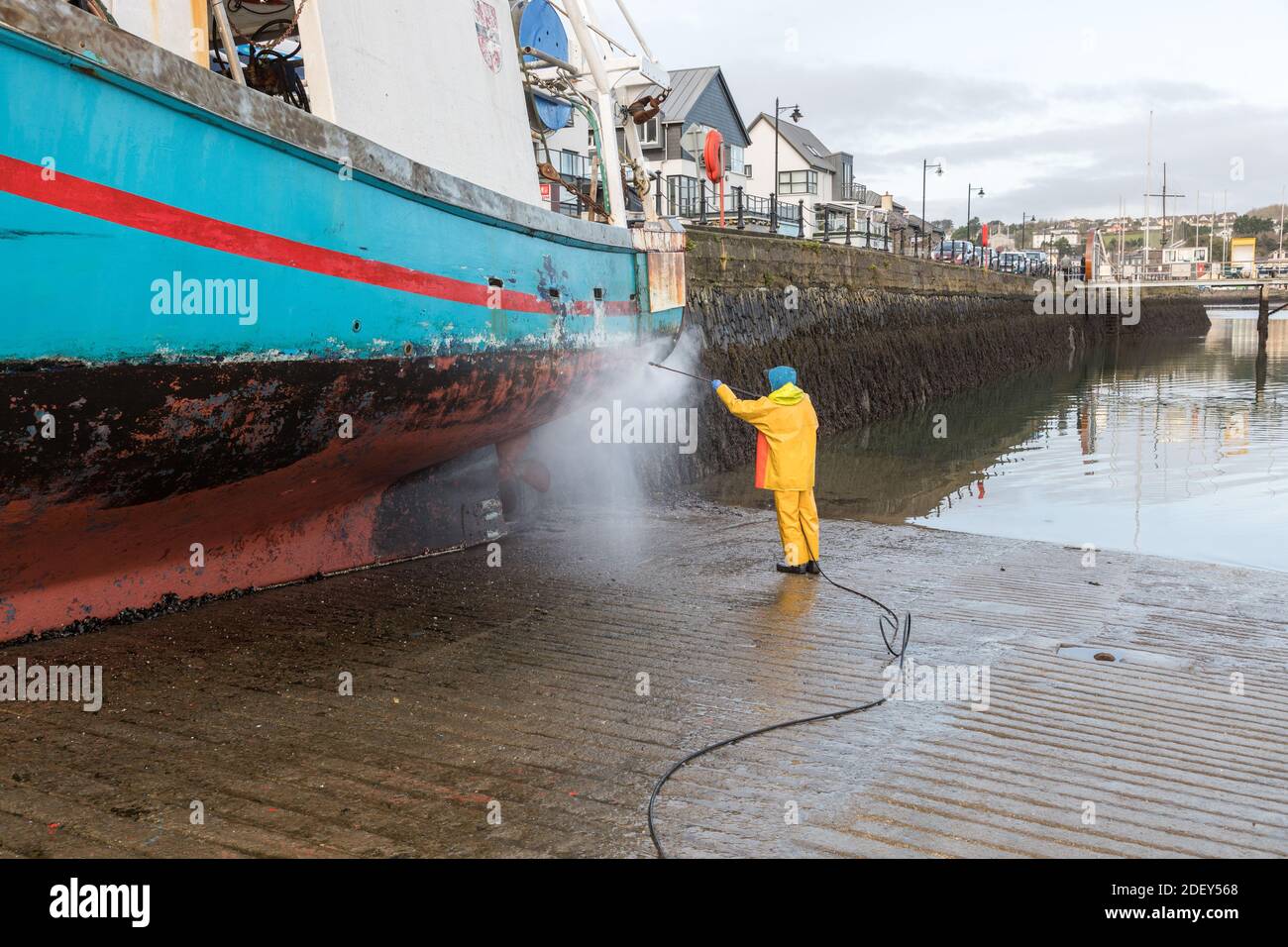 Kinsale, Cork, Irland. Dezember 2020. Fischer Michael McCarthy wäscht den Rumpf seines Fischerbootes 'Aurora Brealis', während er bei Ebbe an der Kaimauer in Kinsale, Co. Cork, Irland, gebunden ist. - Credit; David Creedon / Alamy Live News Stockfoto
