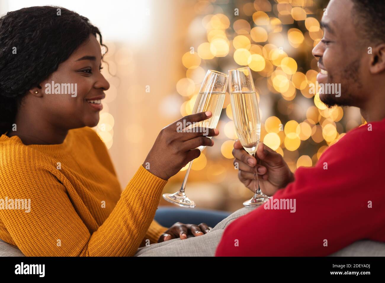 Lächelndes junges afroamerikanisches Paar, das Gläser mit Champagner innen klirrrend Wohnzimmer Stockfoto