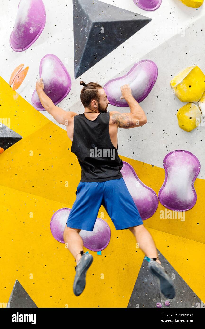 Stock Foto von einem erwachsenen Mann klettern drinnen. Er trägt ein schwarzes Tanktop und blaue Shorts. Er ist nicht erkennbar. Stockfoto