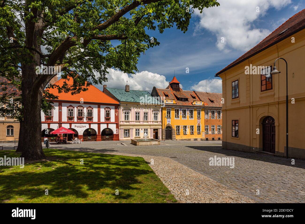 Opocno, Tschechische Republik - Juni 16 2020: Blick auf den Trckovo Platz mit Kopfsteinpflasterstraße, bunten Häusern, einem Brunnen, einem Baum und einer grünen Wiese. Stockfoto