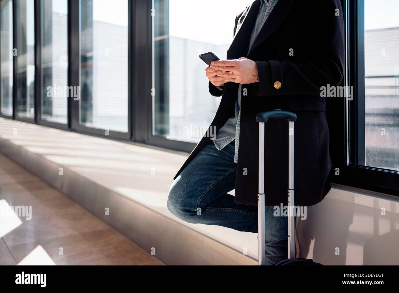 Stock Foto von einer Nahaufnahme von einem nicht erkennbaren Geschäftsmann, der sein Telefon im Flughafen. Er lehnt sich an ein Fenster. Er ist ernst. Er trägt cas Stockfoto