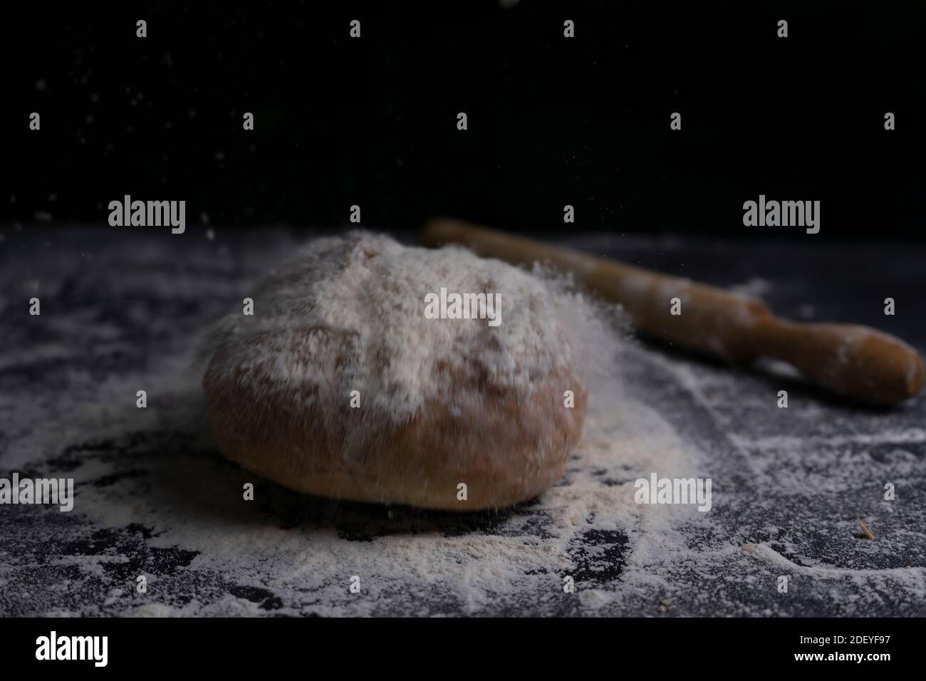 Frisches Brot fliegen mit Mehl Spritzer und Nudelholz auf mehligen schwarzen Tisch.Bäckerei und Backkonzept Hintergrund.Copy Space. Stockfoto