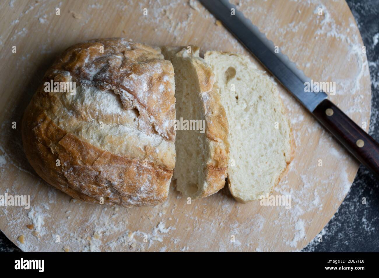 Geschnittenes Weizenbrot mit Mehl und Messer auf Holzbrett.Rustikale Bäckerei, gesunde Ernährung Konzept. Stockfoto