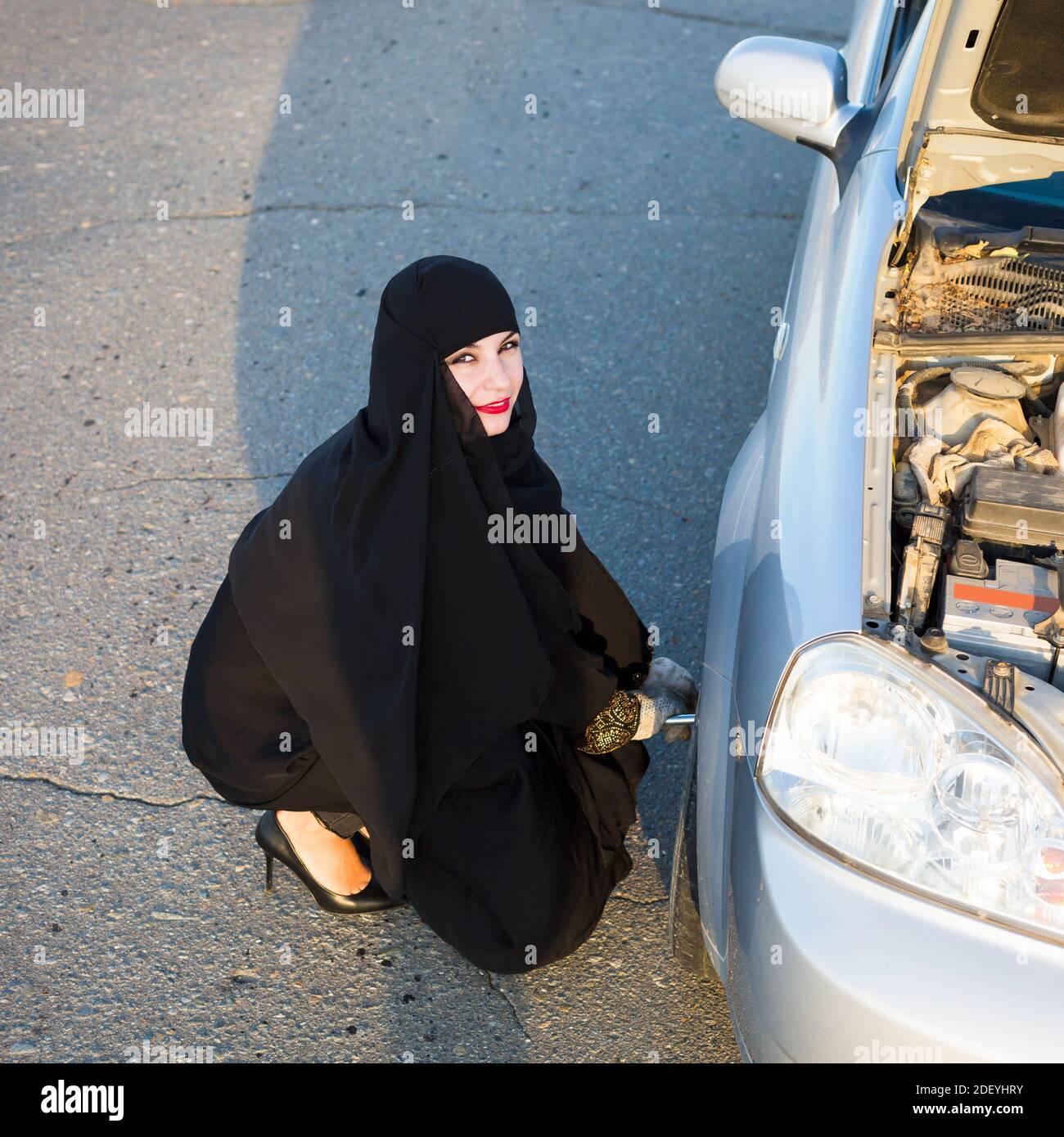 Frau mit einem Lächeln wechselt ein durchstochenes Rad auf dem Auto. Stockfoto