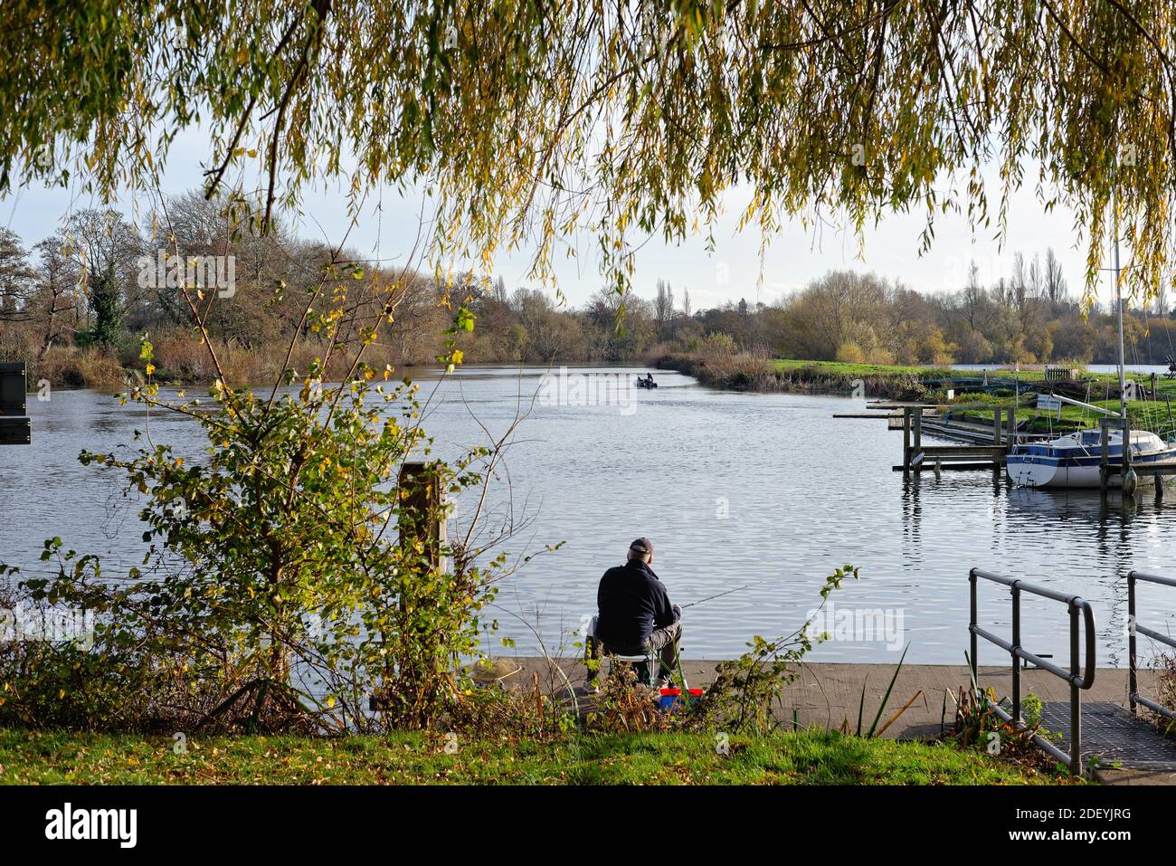 Ein einsamer Fischer, der am Flussufer am Fluss sitzt Thames in Shepperton Surrey England Stockfoto