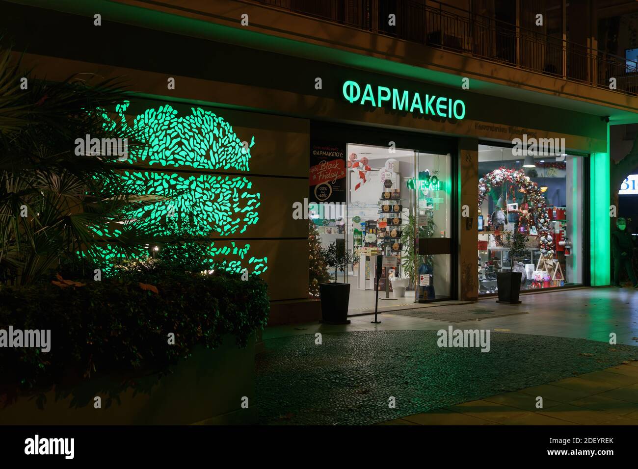 Thessaloniki, Griechenland Griechisch geöffnet Apotheke Eingang. Blick von außen auf den hellenischen Pharmaladen mit beleuchtetem grünen Schild und Schaufenster. Stockfoto
