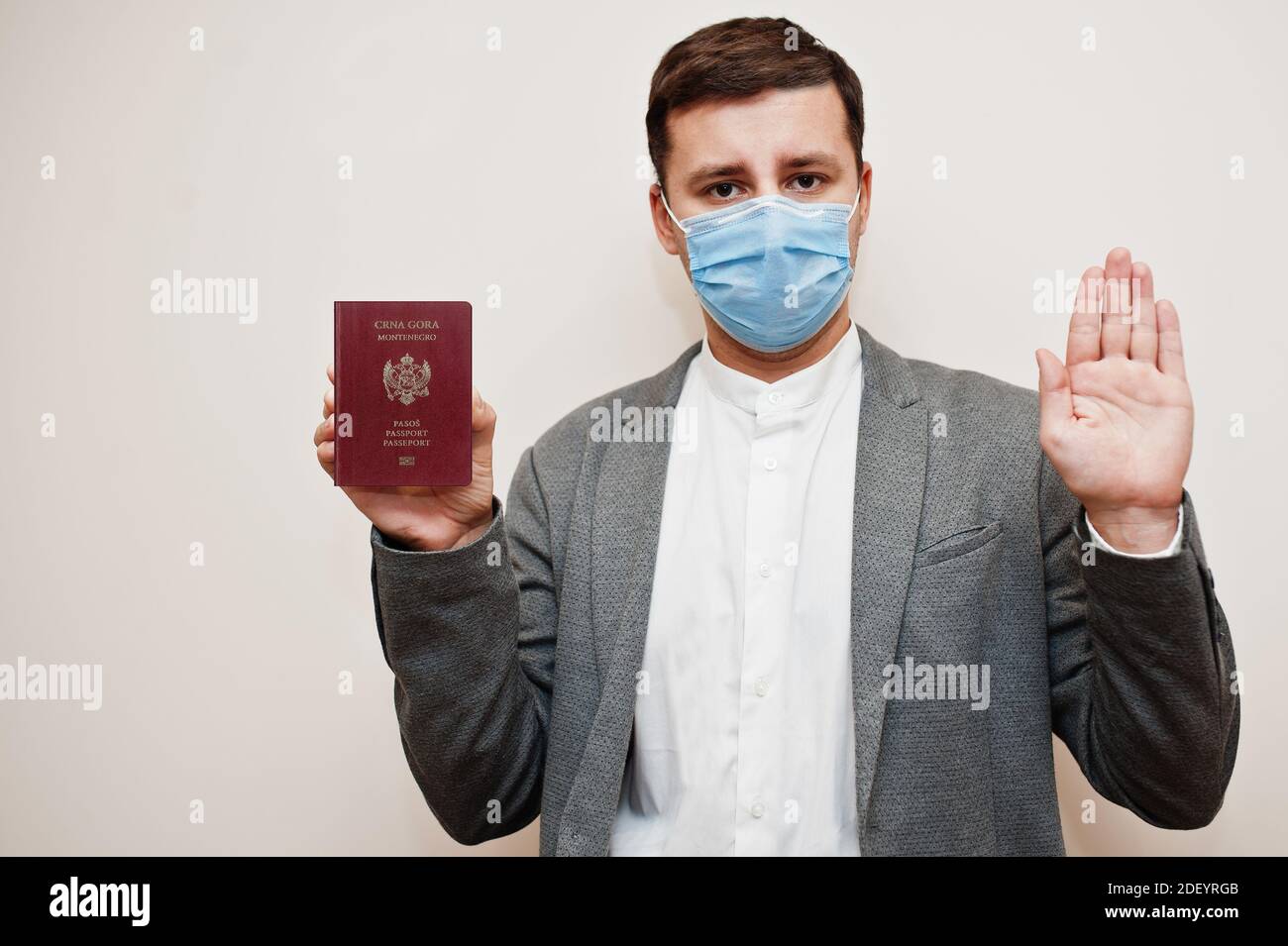 Europäischer Mann in formeller Kleidung und Gesichtsmaske, zeigen AAA-Pass mit Stoppschild Hand. Coronavirus-Lockdown im europäischen Länderkonzept. Stockfoto