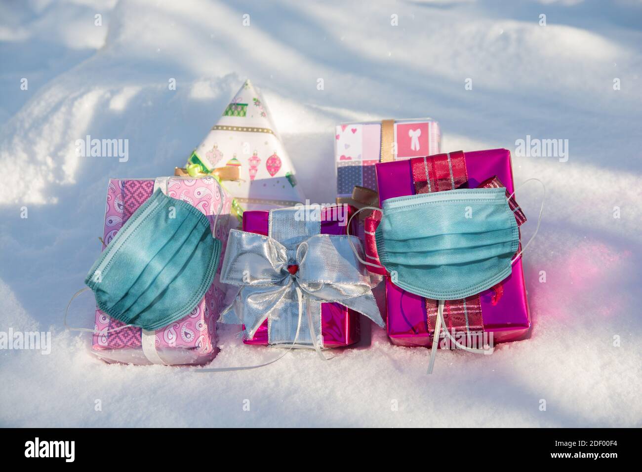 Weihnachten zur Zeit der Corona Pandemie. Weihnachtsgeschenke liegen im Schnee. Gesichtsmasken sind auf den Geschenken. Stockfoto