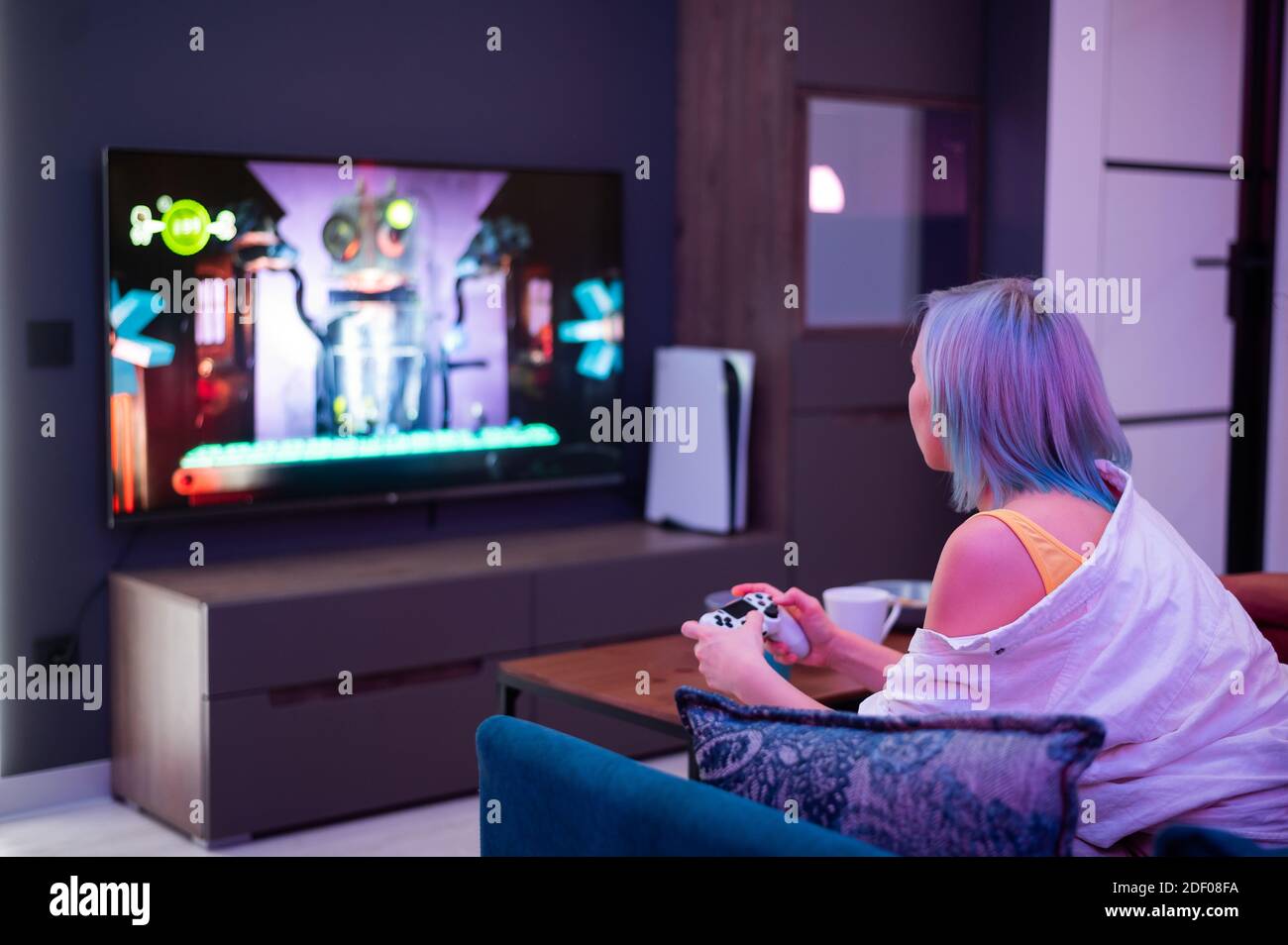 Teenager Mädchen mit bunten blauen und rosa Haaren halten Joystick und spielen Videospiele zu Hause in der Nacht. Stockfoto