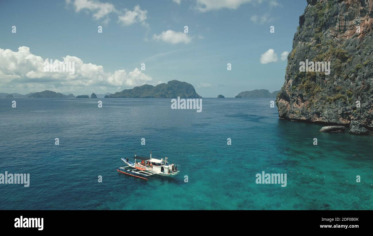 Nahaufnahme Passagierboot in Ocean Bay mit grünen Klippen Ufer in Luftaufnahme. Tropische Meereslandschaft am Sandstrand mit ruhenden Touristen. Nahaufnahme der Hafenlandschaft auf der Insel El Nido, Philippinen, Asien Stockfoto