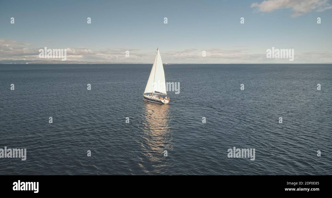 Allein Segelyacht reflektieren an Meereswasser Oberfläche Antenne. Racing Segelboot auf offener See. Luxusschiff bei Sommerkreuzfahrt. Sanftes Sonnenlicht wie im Kino über der weiten, ruhigen Meereslandschaft. Landschaftlich schöne Meeresaufnahme Stockfoto