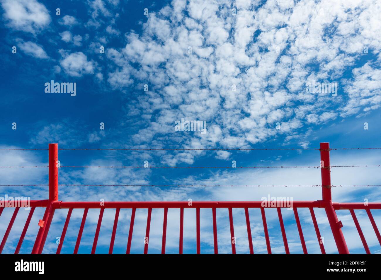 Roter Sicherheitszaun mit Stacheldraht/Rasierdraht gegen blauen Himmel. Stockfoto