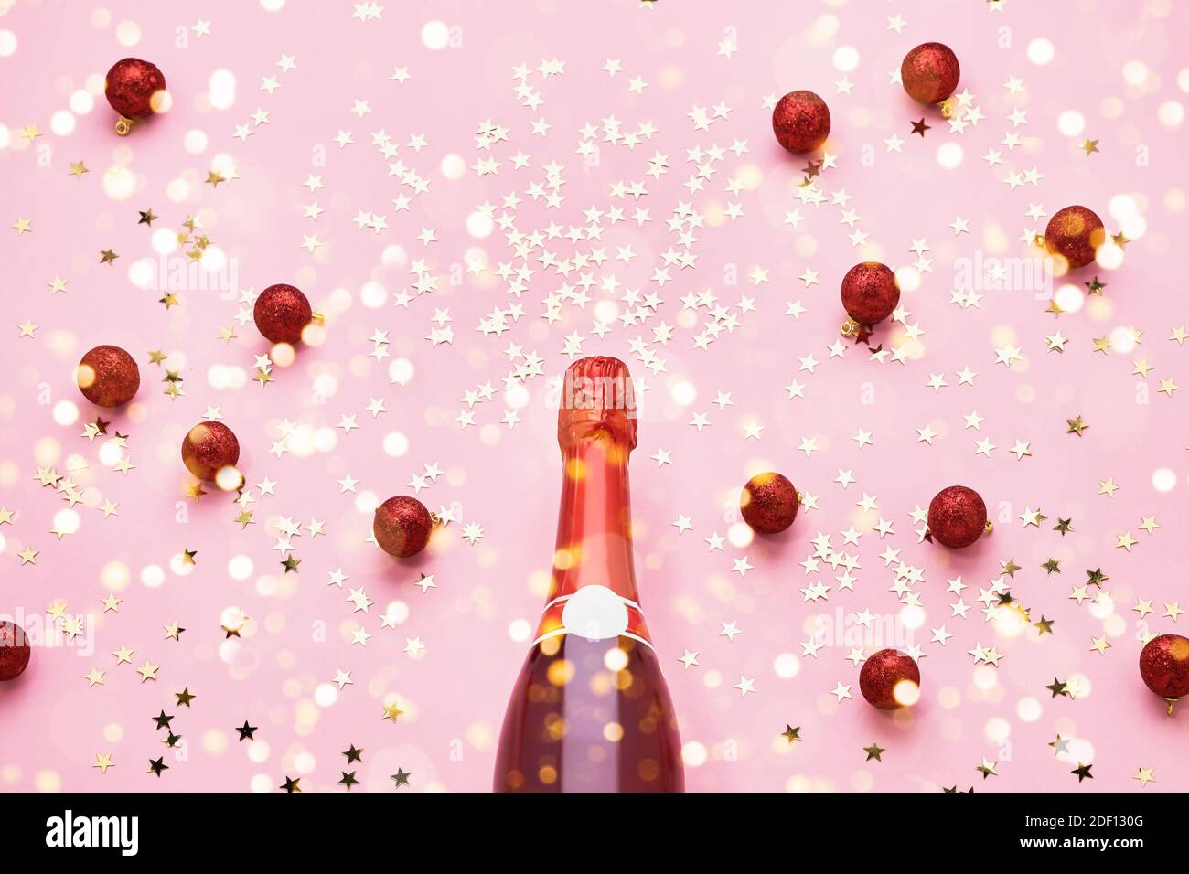 Rote Champagner-Flasche mit roter Weihnachtsdekoration auf rosa Hintergrund. Draufsicht, Kopierbereich Stockfoto