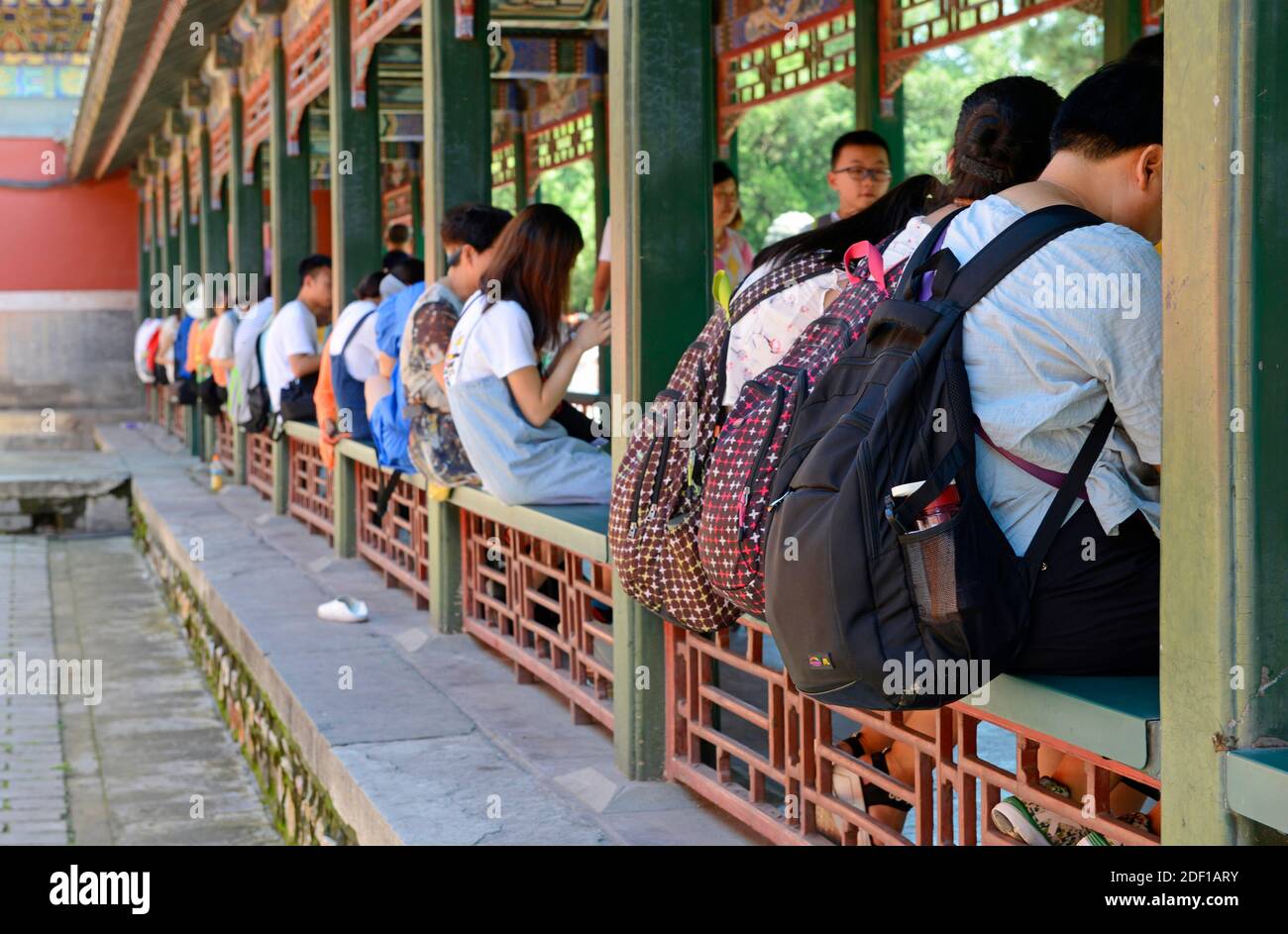 Besucher mit Rucksäcken sitzen auf den Sitzen eines Kreuzgangs im Sommerpalast in Peking, China Stockfoto