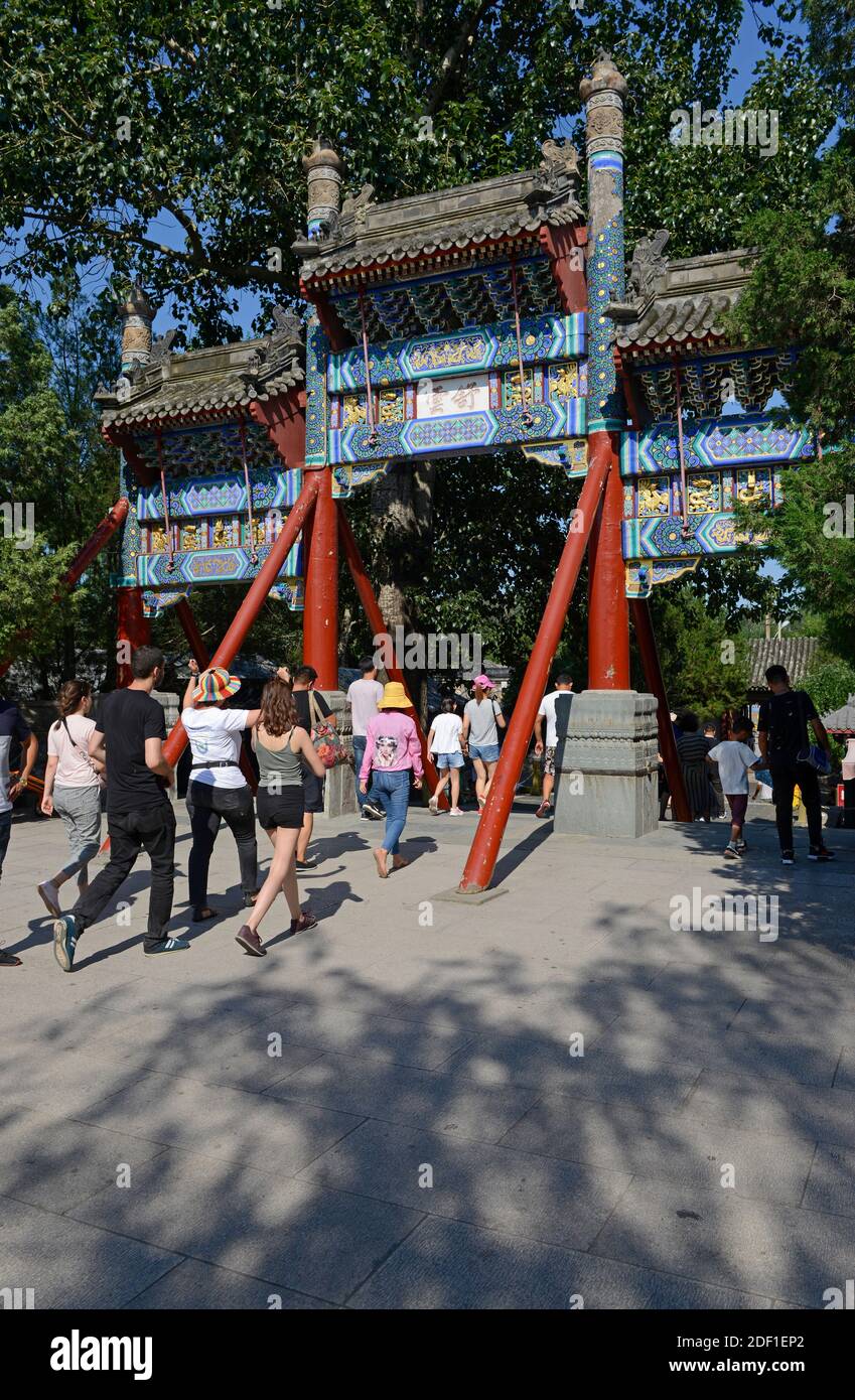 Viele Besucher gehen unter einem traditionellen Tor auf dem Gelände des Sommerpalastes im Nordosten von Peking, China Stockfoto