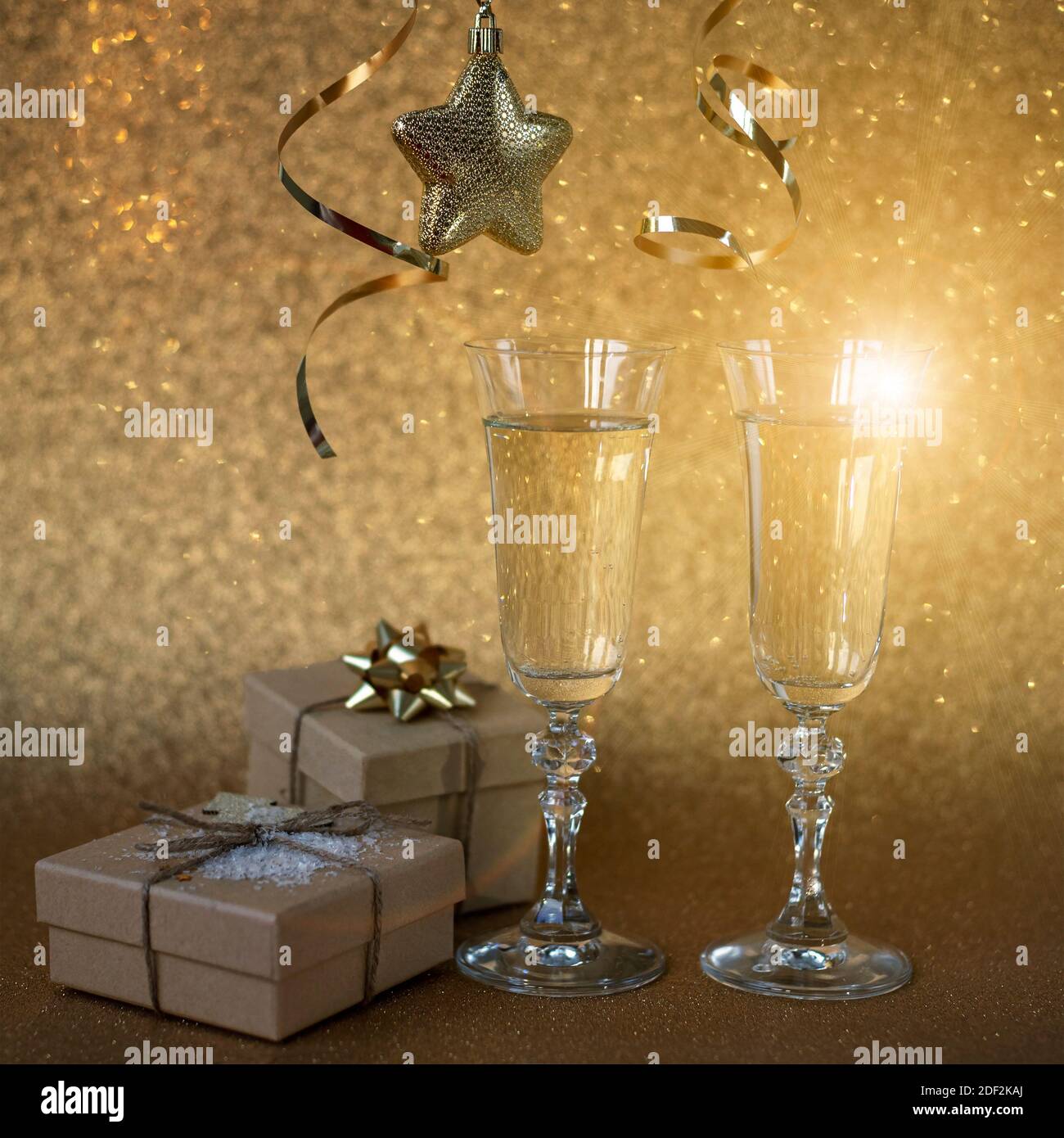 Zwei Gläser Champagner auf goldenem Hintergrund mit weihnachtsgeschenken und -Dekorationen, Nahaufnahme. Neujahrskonzept. Stockfoto