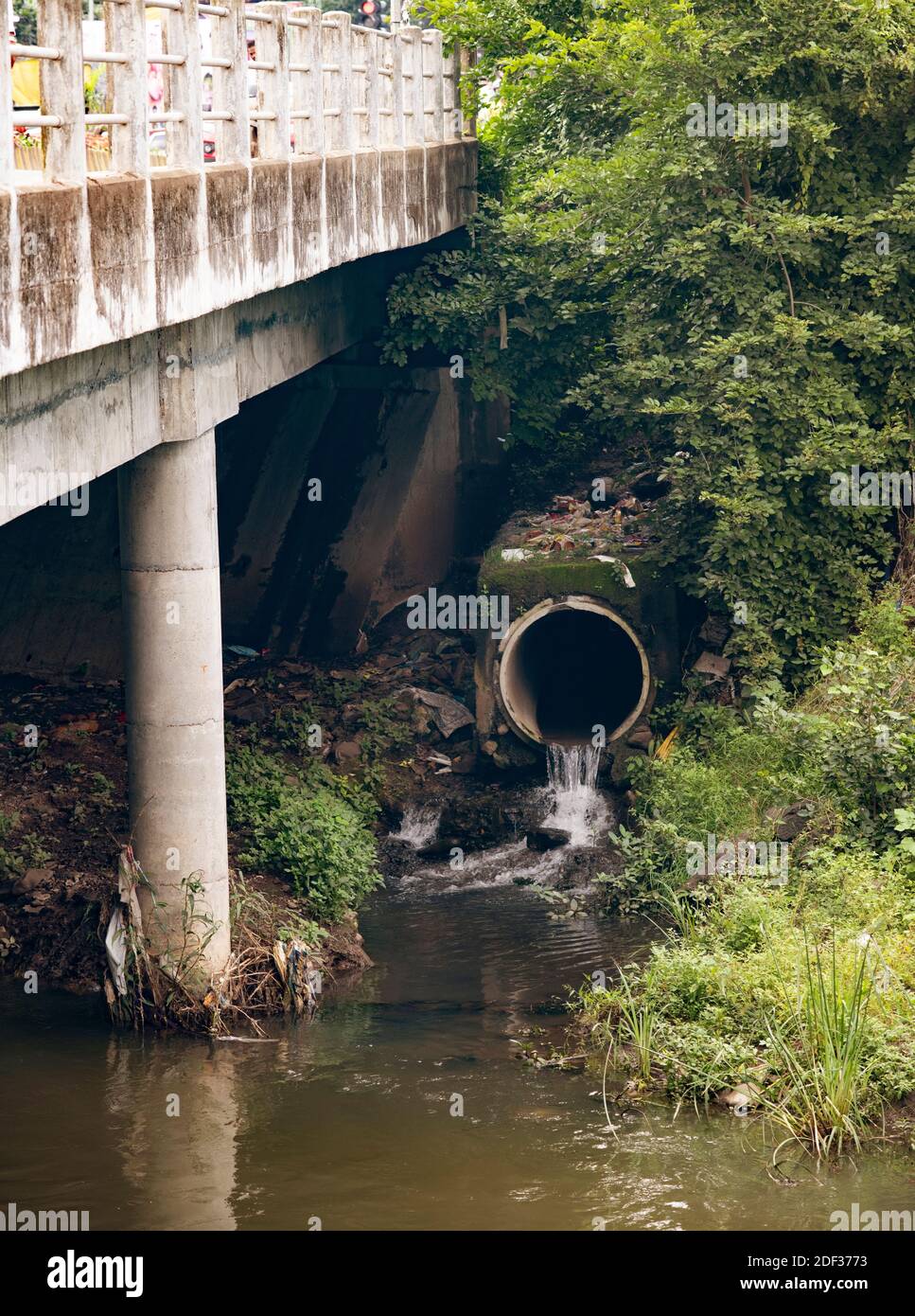 Wasser fließt aus einem kommunalen Sturmabfluss in ein bach unter einer Brücke Stockfoto