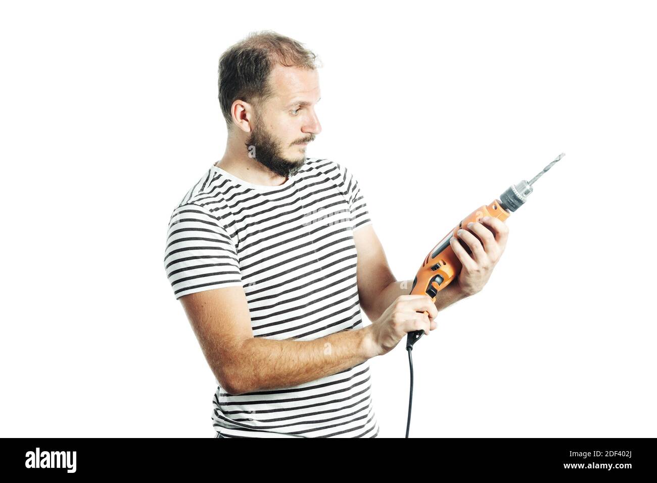 Reifer bärtiger Handwerker, der die Bohrmaschine in seinem betrachtet Hand mit einem fragenden Blick Stockfoto