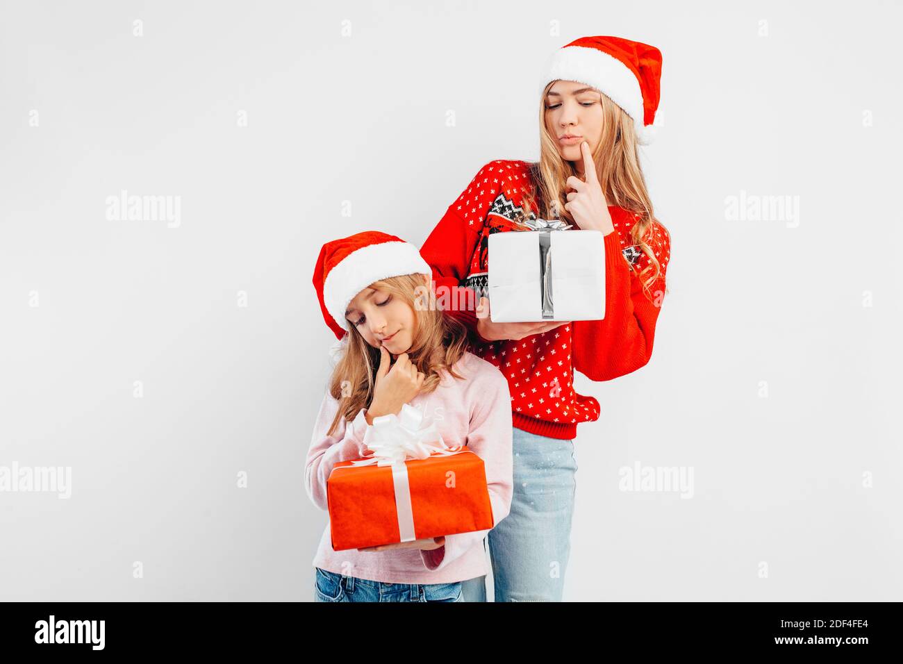 Nachdenkliche Mutter und Tochter, in weihnachtsmützen und Pullover, mit Geschenken in der Hand, auf weißem Hintergrund. Stockfoto