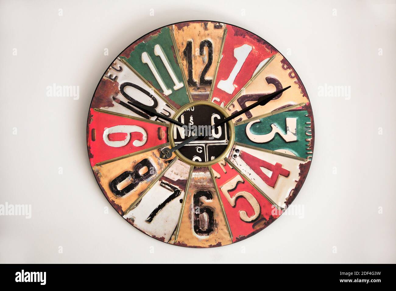 Die Uhr mit Vintage-Metall-Gesicht auf weißer Wand, bezieht sich auf Design der 1930er-50er Jahre, mit Ziffern und Sektoren in verschiedenen Farben Stockfoto