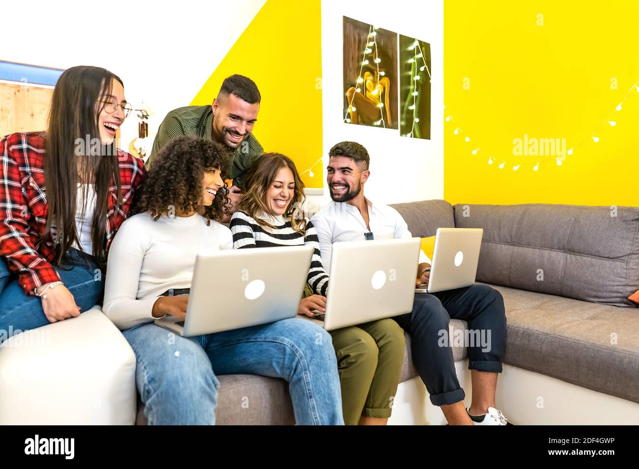Gruppe von Mixed-Rennen Freunde, die Spaß zu Hause in der Wohnzimmer auf dem Sofa sitzend mit Aluminium-Laptop - Junge Leute lächeln zusammen und schauen zu Stockfoto