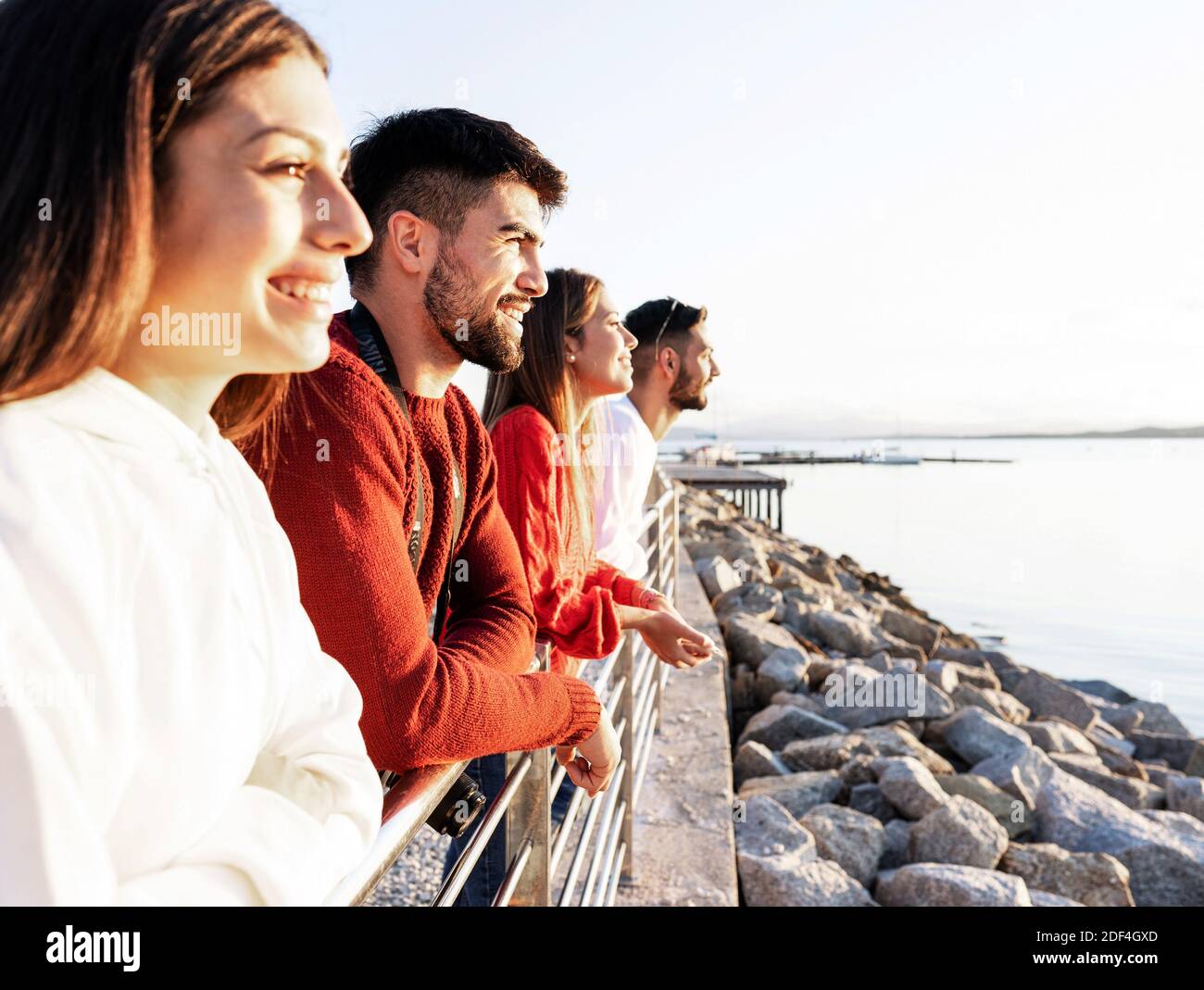 Junge schöne glückliche Menschen, die sich auf ein Metallgeländer stützen Der Sonnenuntergang auf dem Wasser im Meer Winter Urlaubsort - zuversichtlich Freunde Gruppe Blick auf Stockfoto