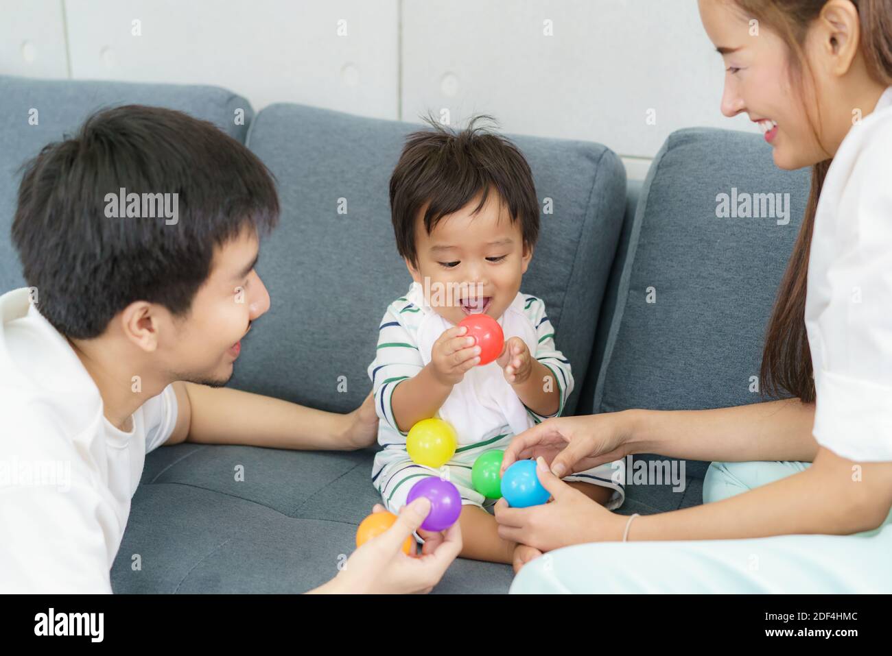 Portrait von asiatischen niedlichen Baby junge spielen bunte Plastikkugeln mit Vater und Mutter auf dem Sofa mit glücklichem Gesicht und lächeln zu lernen Farbe zu Hause. Stockfoto