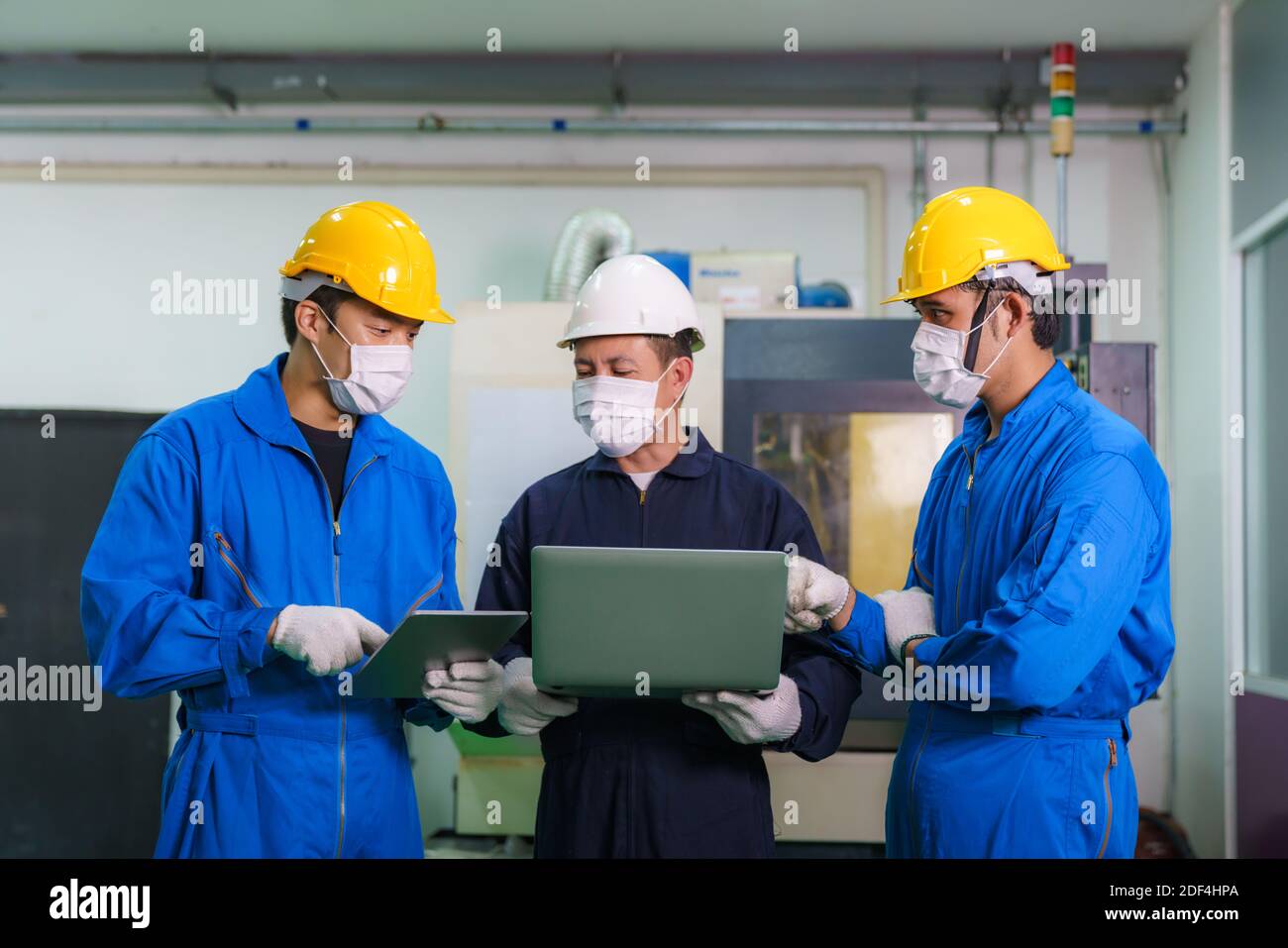 Asiatische Industrieingenieure und Arbeiter in Hartmützen diskutieren Produkt Line in Laptop und machen zeigen Gesten und arbeiten in Eine Schwerindustrie, die produziert Stockfoto