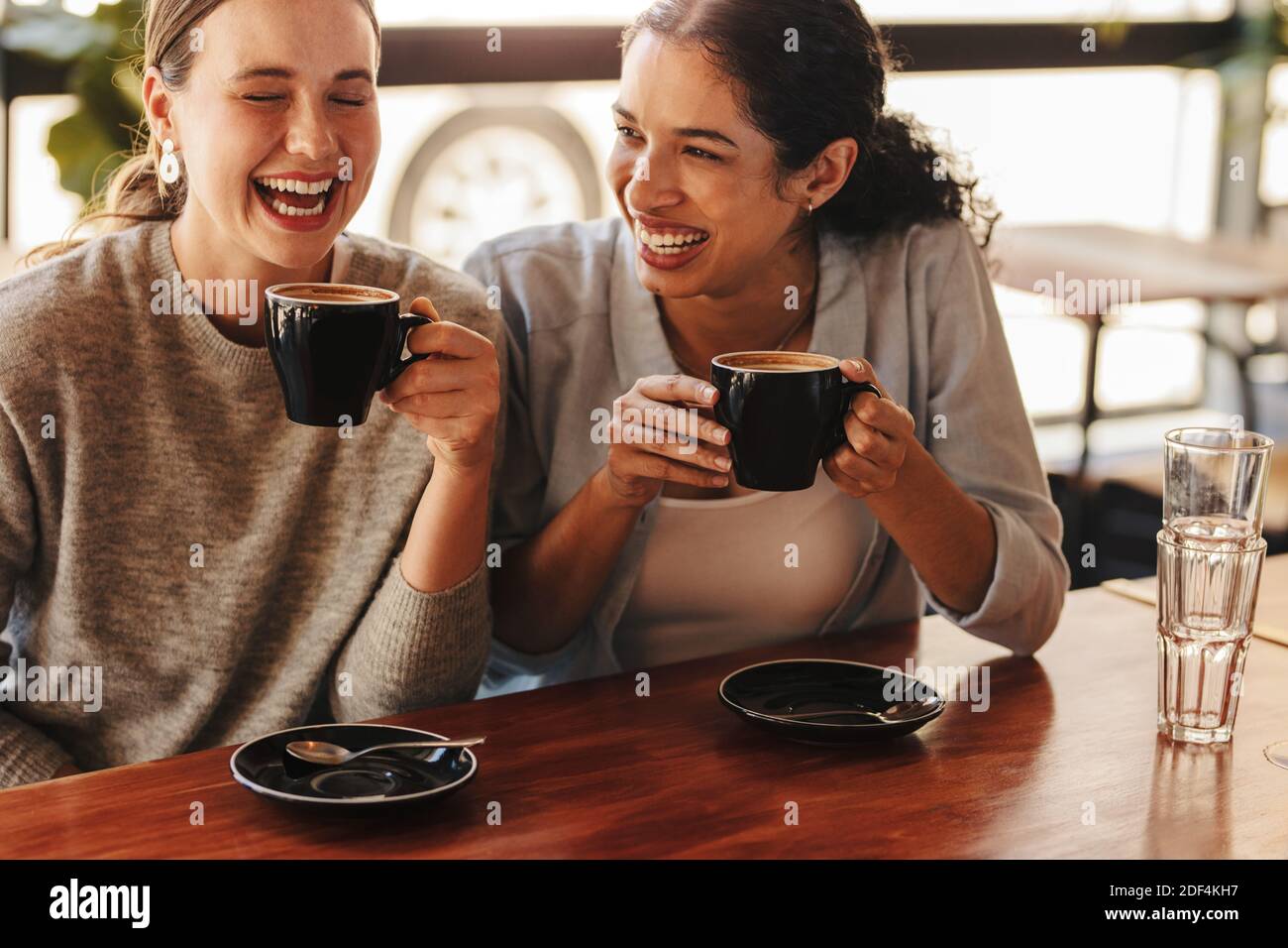 Glückliche Freundinnen in einem Café, die Kaffee trinken. Zwei Frauen sitzen an einem Couchtisch und reden und lachen. Stockfoto