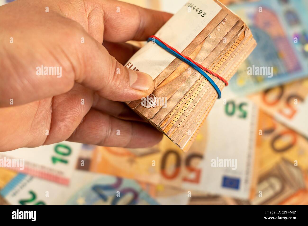 Nahaufnahme der Hand, die eine Rolle von Euro-Geldrechnung auf einem Geldhintergrund hält, Euro-Geld der Europäischen Union Stockfoto