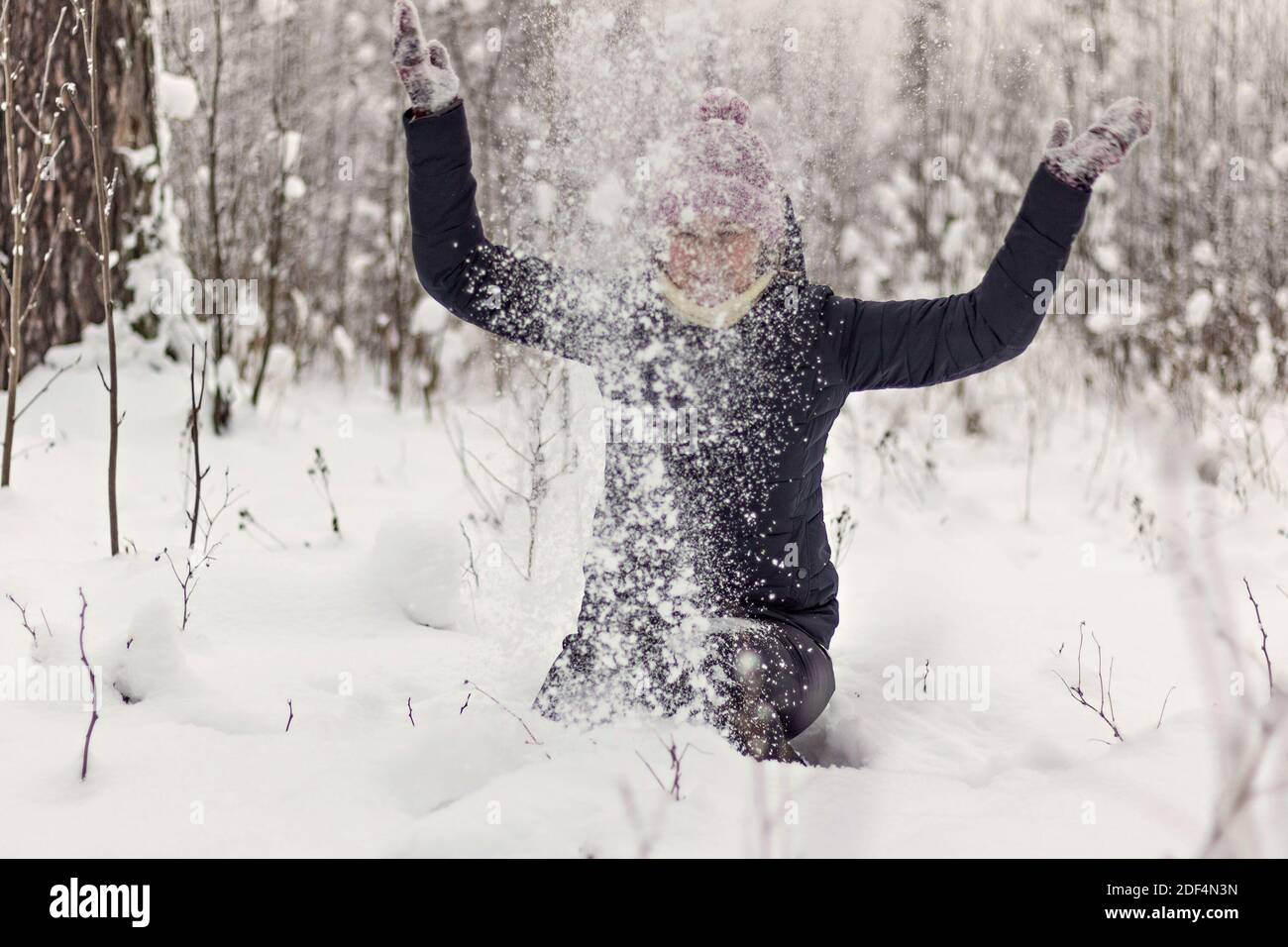 Junge sitzende Frau wirft flauschigen Schnee in den Winterwald. Stockfoto