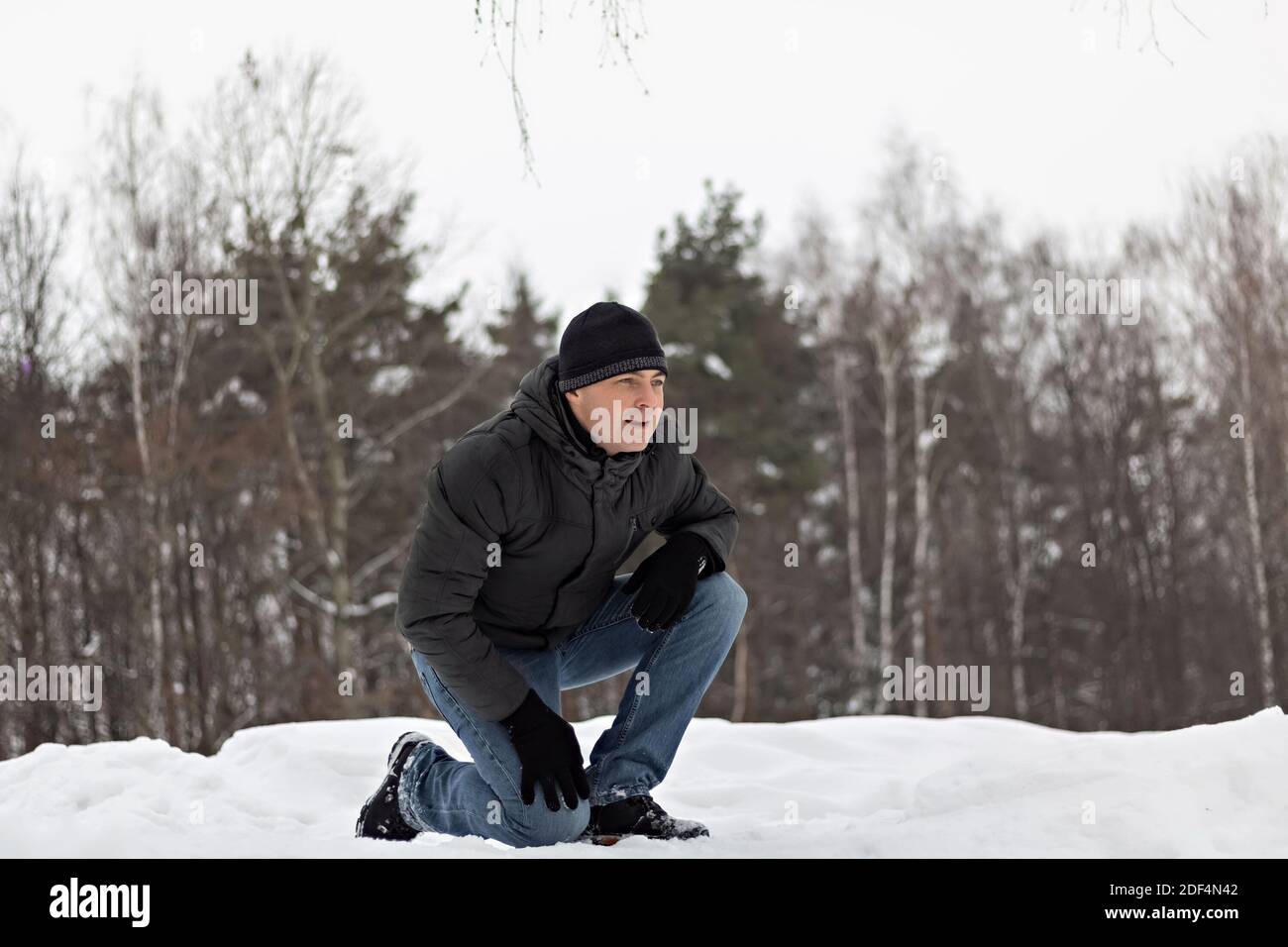 Ein Mann in Winterkleidung ist auf einem Knie im Schnee und spielt mit Kindern. Zeitvertreib für die ganze Familie. Stockfoto